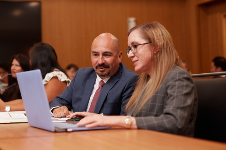 Two staff members sitting in a conference room looking at a laptop screen.